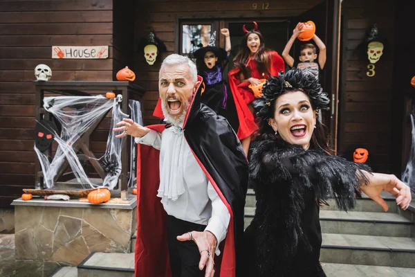 Scared couple in halloween costumes screaming while running out house from creepy kids — Stock Photo