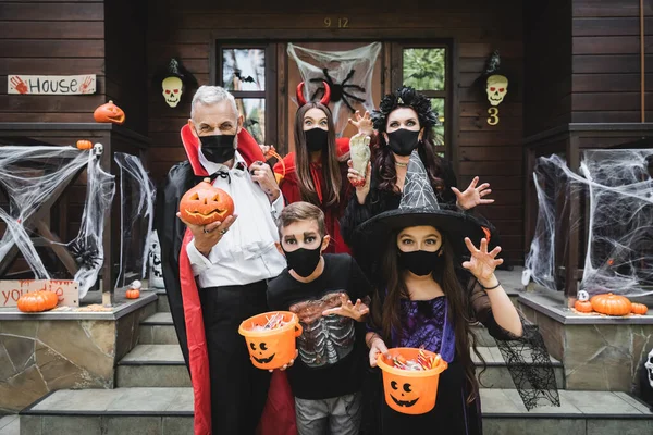 Family in creepy costumes and black medical masks near house with halloween decoration — Stock Photo