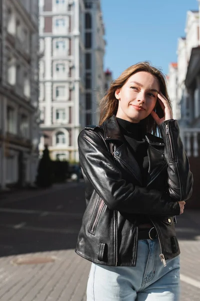 Fröhliche junge Frau in Lederjacke steht auf der Straße — Stockfoto