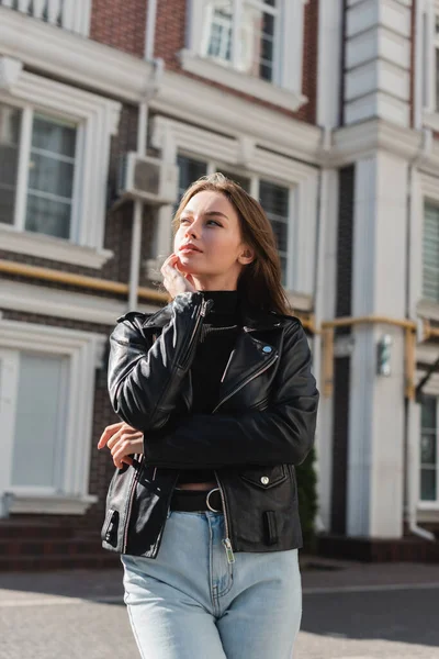 Мрійлива молода жінка в шкіряній куртці, що стоїть на міській вулиці — стокове фото