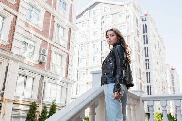 Tiefansicht einer hübschen jungen Frau in schwarzer Lederjacke, die auf einer städtischen Straße in Europa steht — Stockfoto