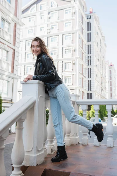 Fröhliche junge Frau in schwarzer Lederjacke steht auf einer städtischen Straße in Europa — Stockfoto