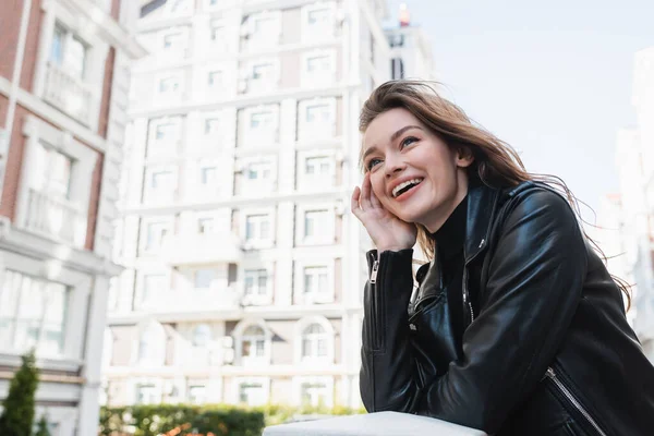 Alegre joven mujer en chaqueta de cuero negro sonriendo en la calle urbana en Europa - foto de stock