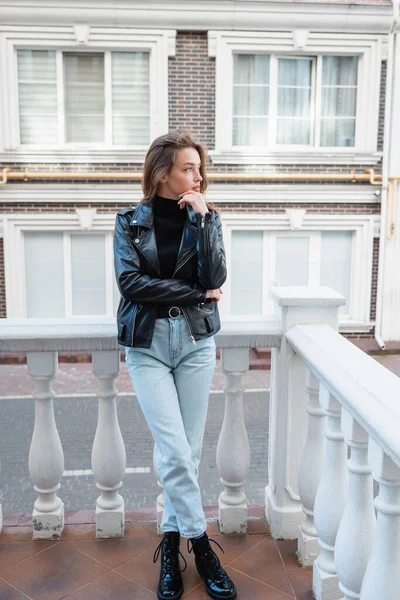 Pleine longueur de jeune femme coûteuse en veste en cuir noir debout sur la rue urbaine en Europe — Photo de stock