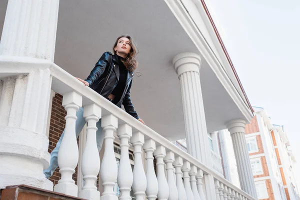 Low angle view of young woman in leather jacket standing on balcony in europe — Stock Photo