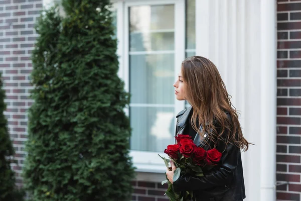 Pretty woman in leather jacket holding red roses on urban street in europe — Stock Photo