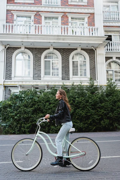 Pleine longueur de femme joyeuse et élégante à vélo sur la rue urbaine de l'Europe — Photo de stock