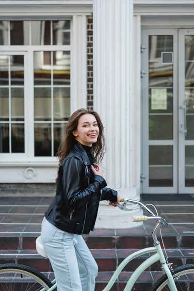 Junge glückliche Frau in stylischer Lederjacke beim Fahrradfahren — Stockfoto