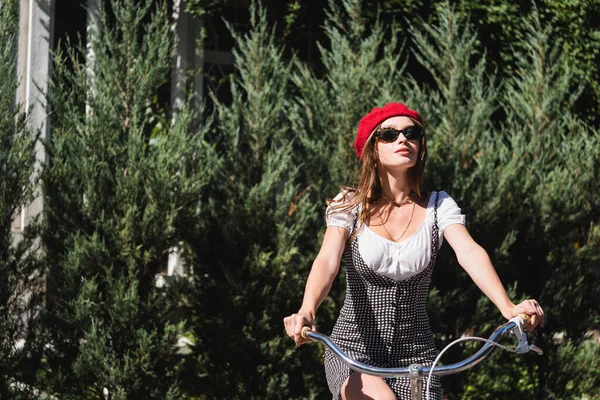Trendy woman sunglasses, red beret and dress riding bicycle outside — Stock Photo