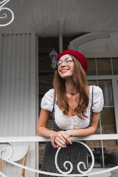 Heureuse jeune femme en béret rouge et lunettes sur le balcon de la maison — Photo de stock