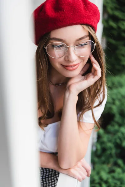 Zufriedene junge Frau mit roter Baskenmütze und Brille, die nach draußen schaut — Stockfoto