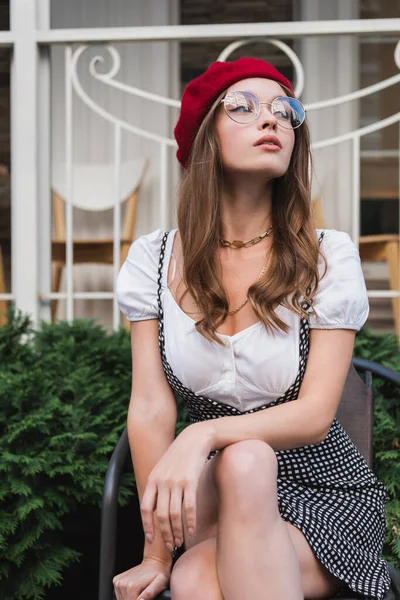 Pretty young woman in red beret and eyeglasses sitting on chair outside — Stock Photo