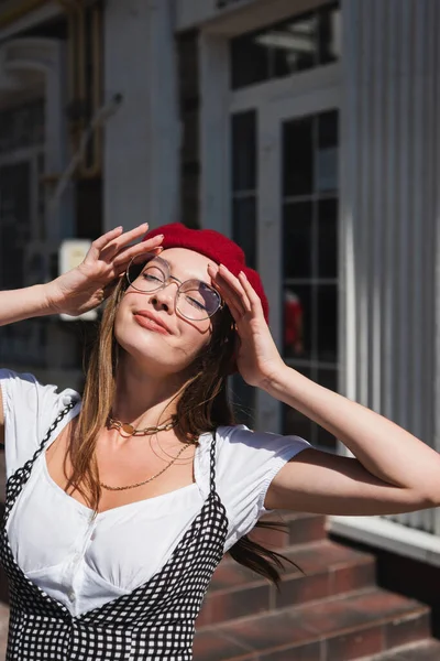 Jovem mulher satisfeita em boina vermelha e óculos desfrutando da luz solar — Fotografia de Stock