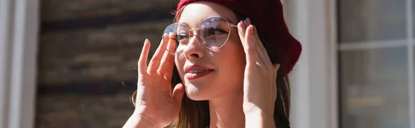 Jovem mulher na boina sorrindo enquanto ajusta óculos, banner — Fotografia de Stock