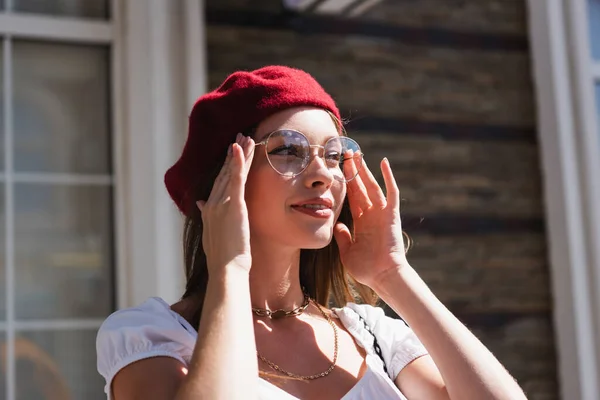 Mujer joven en boina sonriendo mientras se ajustan las gafas - foto de stock