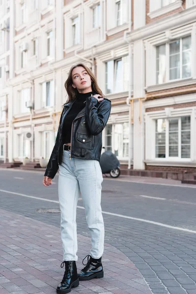 Comprimento total da jovem mulher elegante em gola alta preta e jaqueta de couro na rua urbana da Europa — Fotografia de Stock