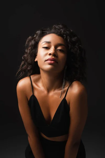 Young african american woman in crop top looking at camera and posing on black — Stock Photo