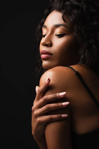 Curly african american woman touching shoulder isolated on black — Stock Photo