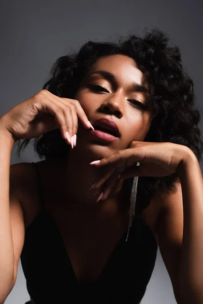 Sexy and young african american woman looking at camera while posing on dark grey — Stock Photo