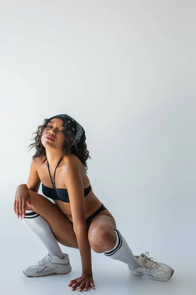 Full length of sexy african american model in swimsuit, knee high socks and sneakers posing on grey — Stock Photo