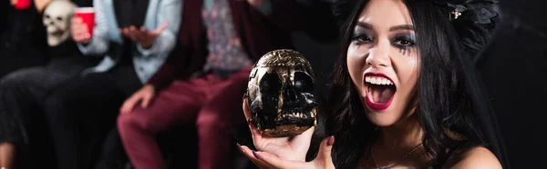 Asiático mujer en vampiro halloween maquillaje mostrando espeluznante cráneo y gruñendo en negro, bandera - foto de stock