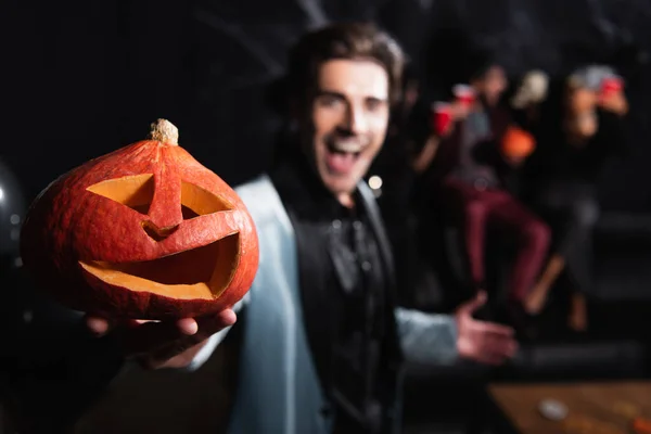 Homem desfocado segurando assustador esculpida abóbora durante festa de Halloween em preto — Fotografia de Stock