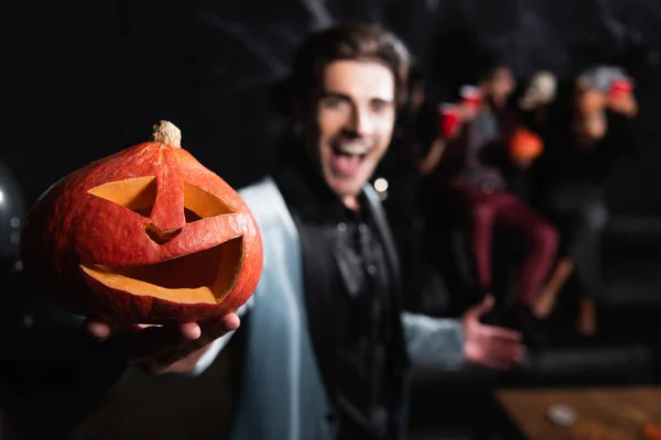 Homme flou tenant fantasmagorique citrouille sculptée pendant la fête d'Halloween sur noir — Photo de stock