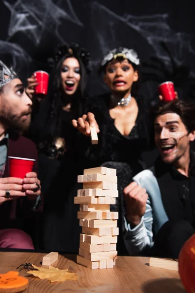 Excited african american woman playing wood blocks game with blurred multiethnic friends on halloween party on black — Stock Photo