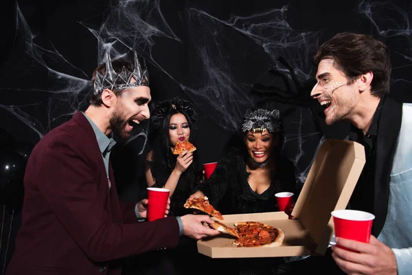 Happy man in vampire king crown taking pizza near multiethnic friends on black — Stock Photo