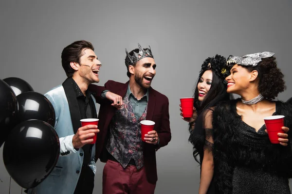 Hombres alegres hablando con mujeres interracial durante la fiesta de halloween aislado en gris — Stock Photo