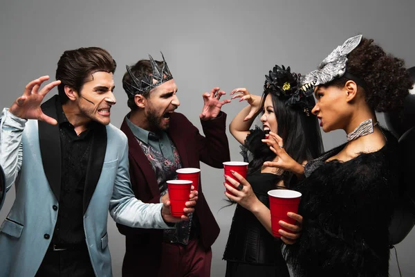 Multiethnic friends in halloween costumes frightening each other isolated on grey — Stock Photo