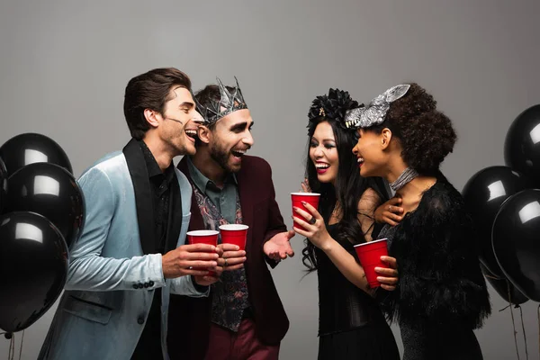 Amigos multiétnicos felices hablando y riendo en la fiesta de Halloween aislado en gris - foto de stock