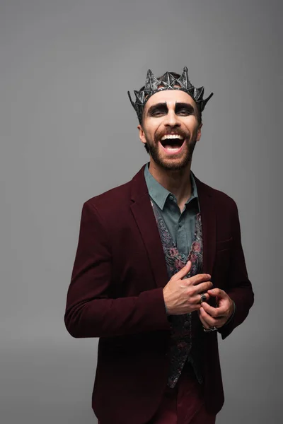 Excited man in vampire king halloween crown laughing at camera isolated on grey — Stock Photo