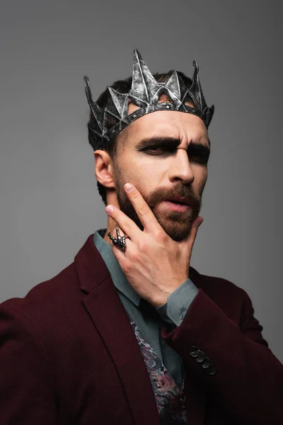 Pensive man in vampire king halloween crown touching chin while looking at camera isolated on grey — Stock Photo