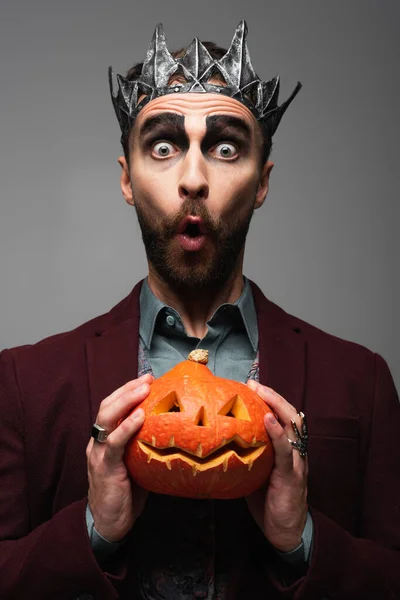 Uomo sorpreso in re vampiro corona tenendo zucca di Halloween isolato su grigio — Foto stock