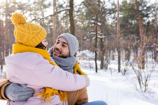 Lächelnder Mann umarmt Freundin in Strickmütze im Winterpark — Stockfoto