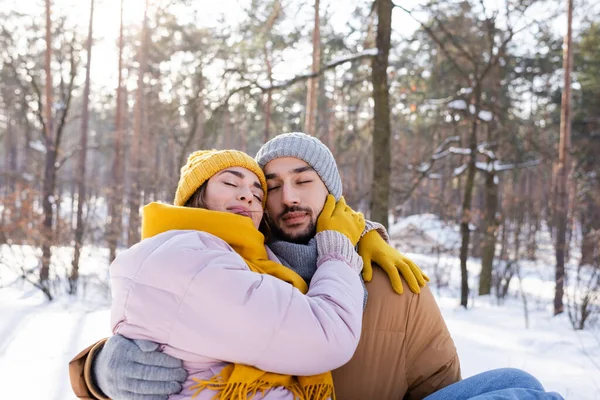 Молодая пара в зимней одежде обнимается с закрытыми глазами в парке — стоковое фото