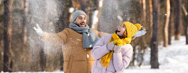 Hombre lanzando nieve cerca de novia emocionada en el parque, bandera - foto de stock