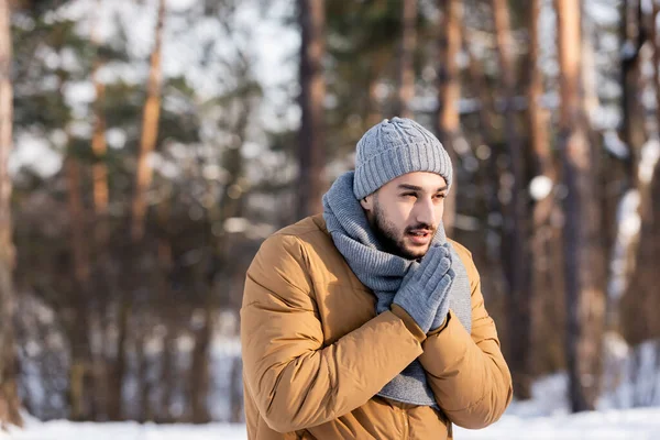 Молодий чоловік в рукавичках і шарфі стоїть в зимовому парку — стокове фото