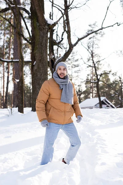 Fröhlicher Mann mit warmem Schal und Hut steht im verschneiten Park — Stockfoto