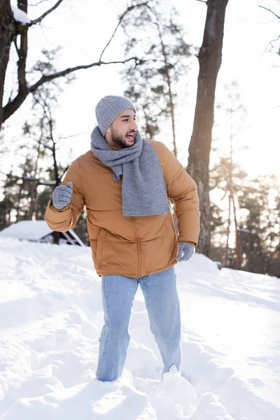 Positiver Mann mit Hut und Schal schaut im Schnee im Freien weg — Stockfoto