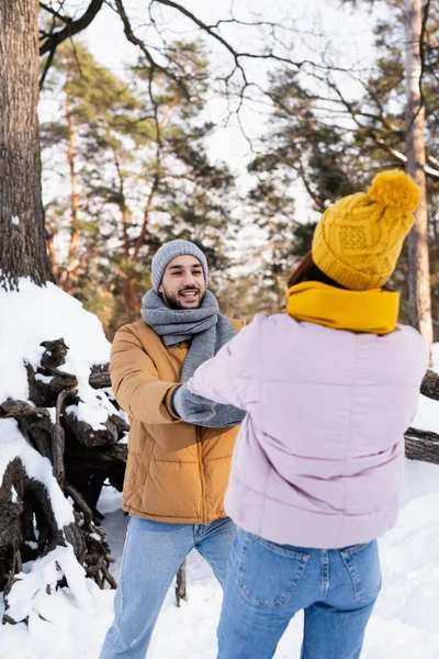 Cheerful man holding hand of girlfriend on blurred foreground in winter park — Stock Photo