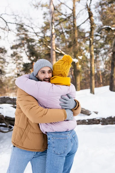 Uomo sorridente che abbraccia la ragazza in abito invernale nel parco durante il giorno — Foto stock