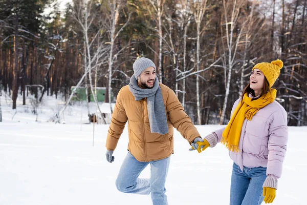 Веселый мужчина держит за руку взволнованную девушку в зимнем парке — стоковое фото