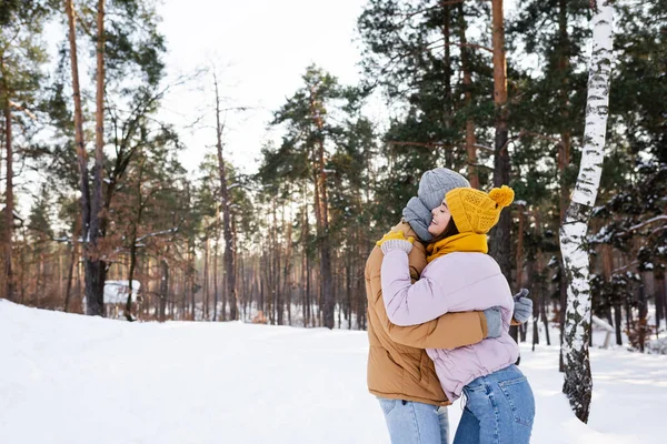 Vista lateral de la mujer sonriendo y abrazando novio en el parque de invierno - foto de stock