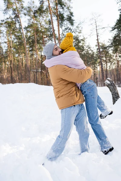 Feliz hombre levantando novia en la nieve en el parque de invierno - foto de stock