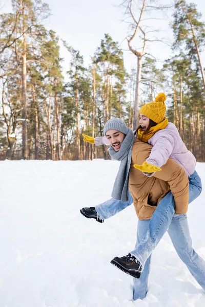 Mulher excitada piggybacking no namorado no parque de inverno — Fotografia de Stock