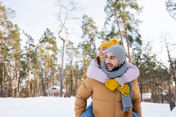 Smiling woman piggybacking on boyfriend in winter park — Stock Photo