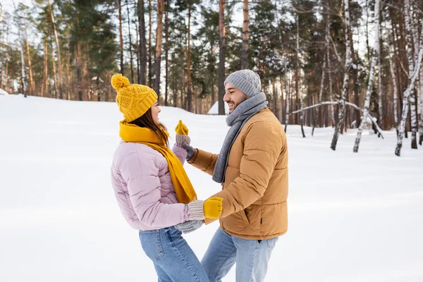 Side view of cheerful coupe in winter outfit dancing in snowy park — Stock Photo
