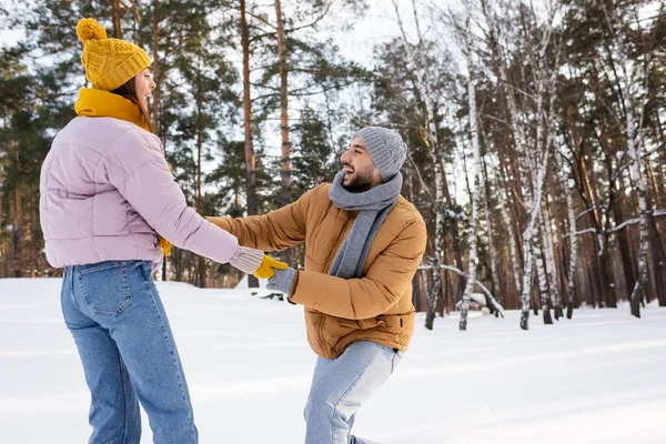 Seitenansicht eines aufgeregten Mannes, der die Hände seiner Freundin in Handschuhen im verschneiten Park hält — Stockfoto